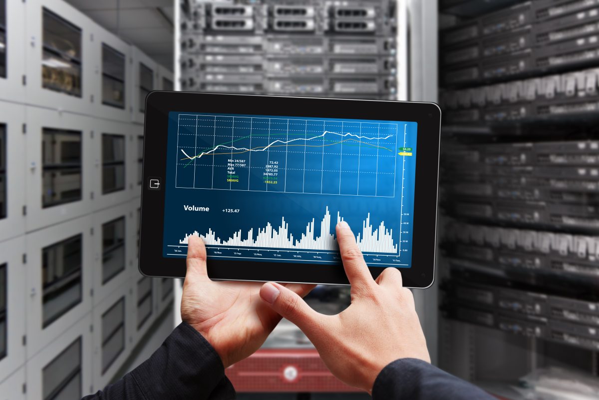 Händer håller en surfplatta med grafer över trafikvolym framför serverrack i ett datacenter, en bild för att matcha webbutikens trafik mot hostingens kapacitet
