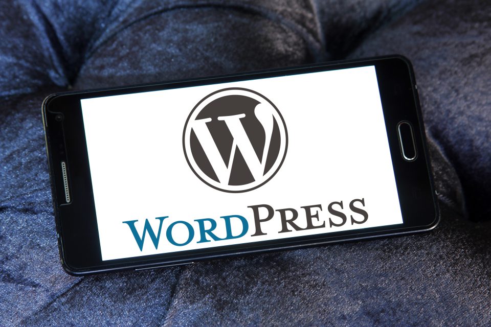 WordPress-logotypen på skärmen till en smartphone som ligger på mörkblått tyg